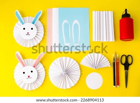 On a yellow background, the layout of the crafts.  Cute, cute Easter white rabbit made of paper.  The concept of spring, Easter holiday, children's creativity.  Flat lay, top view.