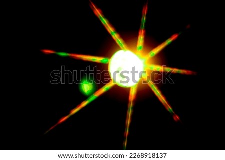 blurred bokeh in the shape of a star of bright psychedelic neon colors of light green orange yellow and red on a dark background.
