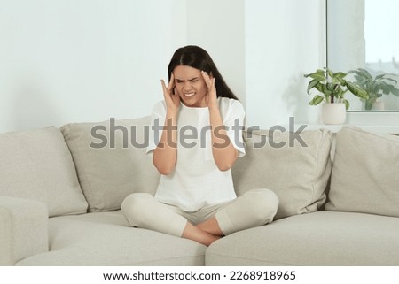 Young woman suffering from headache on sofa at home. Hormonal disorders Royalty-Free Stock Photo #2268918965