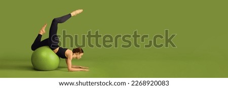 Young slim fit girl doing stretching exercises with fitness ball over green studio background. Concept of sport, body care, beauty, fitness, active lifestyle. Banner. Copy space for ad Royalty-Free Stock Photo #2268920083
