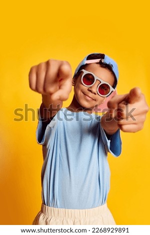 Closeup portrait of little african happy boy in stylish sunglasses and cap looking at camera over bright yellow background. Concept of music, happiness, kids emotions and ad Royalty-Free Stock Photo #2268929891
