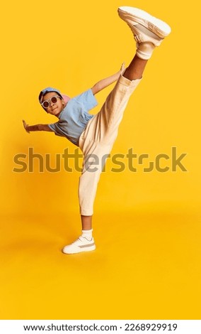Dynamic portrait of little african boy, hip-hop dancer in stylish street style clothes dancing over bright yellow background. Concept of music, dance happiness. Kid looks happy and sportive Royalty-Free Stock Photo #2268929919