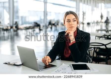 Photo of a pensive thoughtful elegant caucasian business woman, executive, recruitment, product manager, sits in a business center, working in a laptop, tired looking away, thinking, dreaming Royalty-Free Stock Photo #2268941839