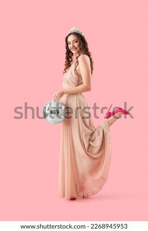 Beautiful young woman in prom dress and with disco ball on pink background