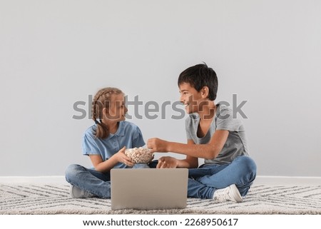 Little boy and his sister with popcorn watching cartoons on laptop near light wall