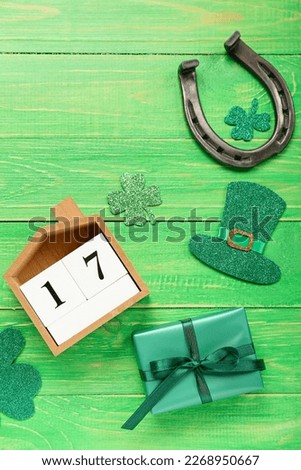 Calendar with date of St. Patrick's Day, horseshoe, gift and decor on green wooden background