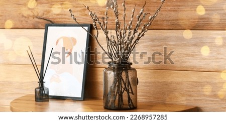 Vase with willow branches and picture near wooden wall in room