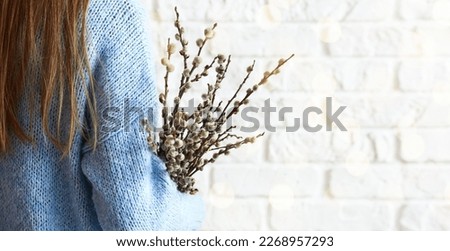 Woman holding willow branches on white brick background, closeup. Banner for design