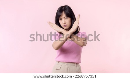 portrait young serious asian woman with cross arm gesture showing stop, no, wrong, denial, rejection sign isolated on pink pastel studio background. deny and negative expression symbol concept.