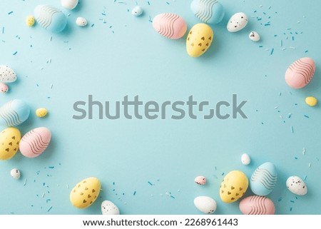 Easter decor concept. Top view photo of yellow pink blue easter eggs and sprinkles on isolated pastel blue background with blank space in the middle Royalty-Free Stock Photo #2268961443
