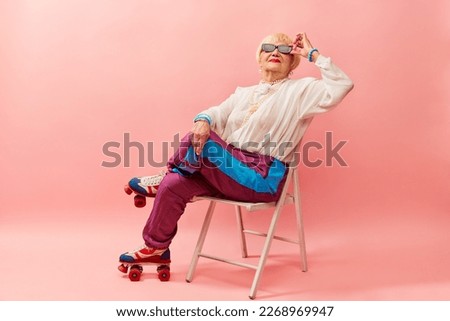 Relaxed vibe. Beautiful old woman, grandmother in stylish sportive trousers posing on vintage rollers over pink studio background. Concept of age, fashion, lifestyle, emotions, facial expression Royalty-Free Stock Photo #2268969947