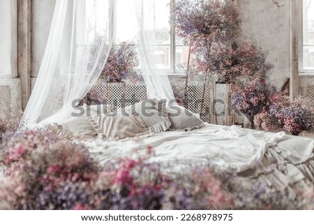 A bed in a bright bedroom in pastel colors in boho style, the trending color of 2023. The room is decorated with lilac and pink gypsophila flowers, vintage decor in the room in retro loft style.