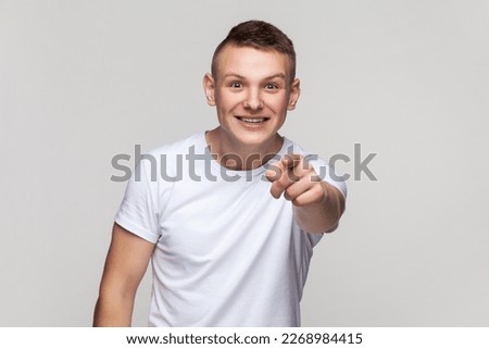 Portrait of astonished surprised young teenager boy wearing T-shirt looking at camera with big eyes, pointing at camera with finger, choosing you. Indoor studio shot isolated on gray background.