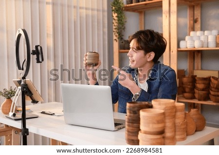 A young Asian man entrepreneur live streaming to sale craft products  to customers in his shop , Technology online business concept. Royalty-Free Stock Photo #2268984581