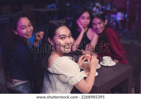 Four lovely Southeast Asian ladies dining in a tavern with live band. Emphasis on a young beautiful woman dressed in a white puffed top beaming at the camera while eating seafood dishes. Royalty-Free Stock Photo #2268985395