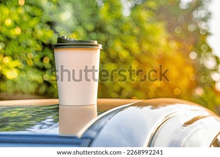 coffee takeaway in a paper cup on top of the car roof green tree background at sunrise in the morning,  selective focus, soft focus. Royalty-Free Stock Photo #2268992241
