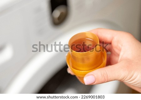Female hand holding light brown bottle cap with liquid soap, close up. Concept of washing clothes, household tasks, cleaning and laundry Royalty-Free Stock Photo #2269001803