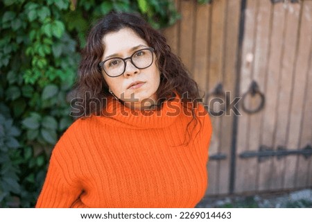 Portrait of carefree young woman smiling with big door background. Cheerful latin girl wearing eyeglasses in the city copy space. Happy brunette woman with curly hair and spectacles smiling. Copy