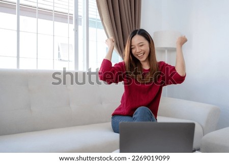 Happy young Asian business woman successful excited raised hand rejoicing with laptop at home.