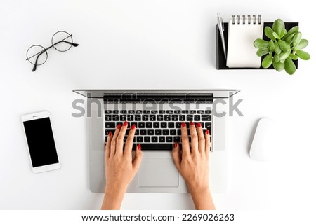 Overhead shot of woman’s hands working on laptop on white table with accessories. Office desktop. Flat lay
