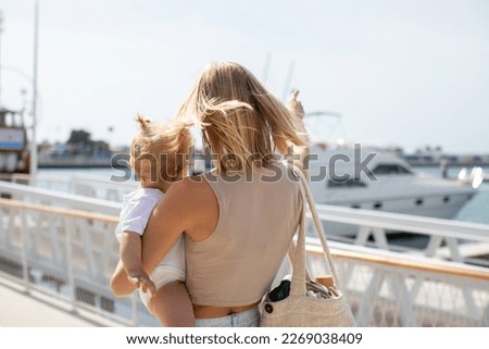A woman carries a child in her arms walking along the marina. Mother and daughter.