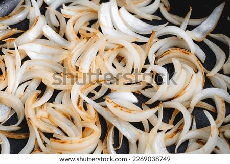 Close Up View of Sliced Onions Browned in a Skillet: Slices of sweet onion cooked in olive oil browning in a frypan Royalty-Free Stock Photo #2269038749