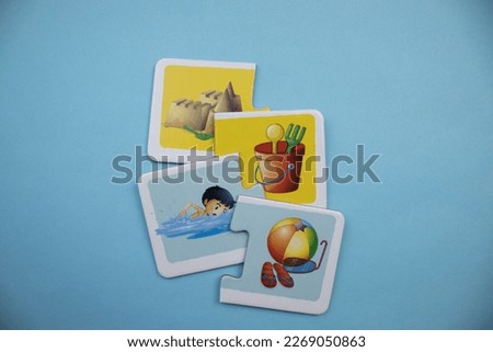 Picture puzzle pieces of sand castle, bucket, swimming boy and beach equipment placed on blue background.