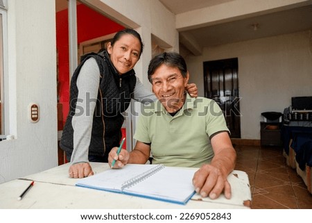 Hispanic adult couple studying together - teacher teaching senior to write - couple budgeting at home Royalty-Free Stock Photo #2269052843