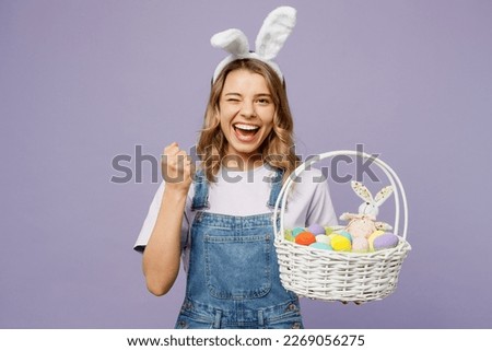 Young cool fun woman wearing casual clothes bunny rabbit ears hold wicker basket colorful eggs do winner gesture isolated on plain pastel light purple background studio portrait. Happy Easter concept