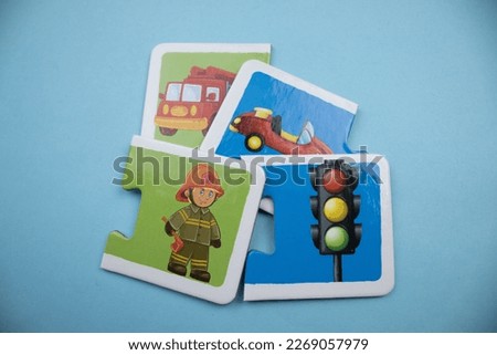 Picture puzzle pieces with fire engine, car, traffic signs and firefighter placed on blue background.