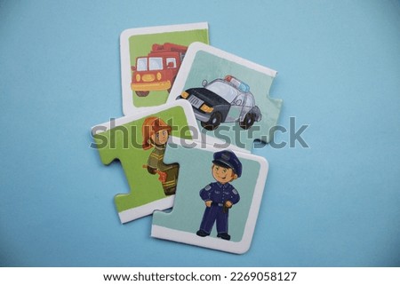Puzzle pieces with picture of fire engine, police car, fireman and policeman placed on blue background.