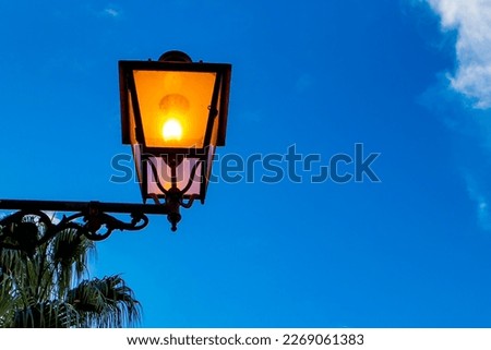 Old-fashioned Street Lamp in the Evening. A Brightly lit Street Lamp on a building in Italy. Decorative lamps. Magic Lamp with Warm Yellow Light in Urban Twilight. Copy Space.
