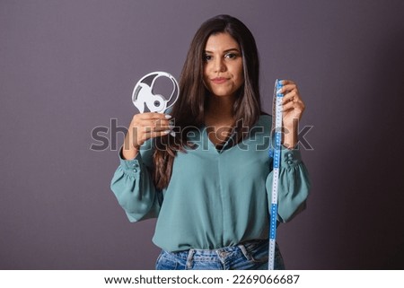 Horizontal photo. Beautiful Brazilian woman, with casual clothes, Jeans and green shirt. nutritionist holding measuring tape and adipometer