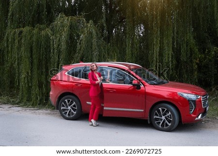 A woman in a red Chinese car drinks coffee in a business suit. Online work in nature. Freelance, travel, remote work. Freedom of movement, model in the forest. High quality photo