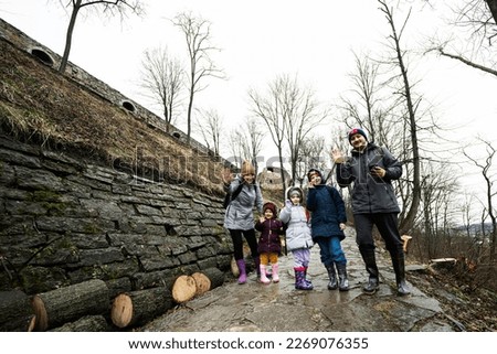 Family tourist with three children stand on wet path to an ancient medieval castle fortress in rain.
