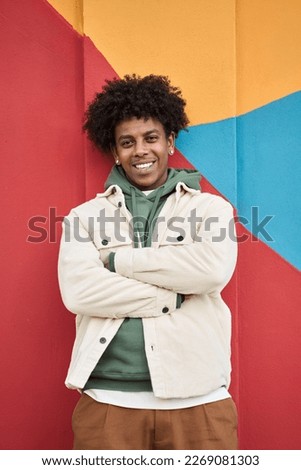 Young happy African American teen guy isolated on bright vibrant city wall background. Smiling cool ethnic generation z teenager boy student model standing looking at camera, vertical portrait.