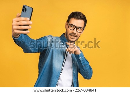 Cheerful young business man in hat taking selfie with smartphone isolated over yellow background.