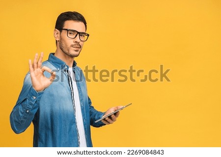 Serious bearded man using digital tablet looking shocked about social media news, astonished man shopper consumer surprised excited by online win isolated over yellow background. Ok sign.