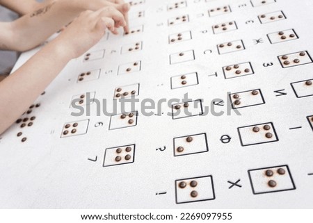 Braille font on a white metal plate with Ukrainian translation. The child's hand touches the convexity of the plate. Tactile reading of the letters of the Ukrainian alphabet (Cyrillic) in Braille