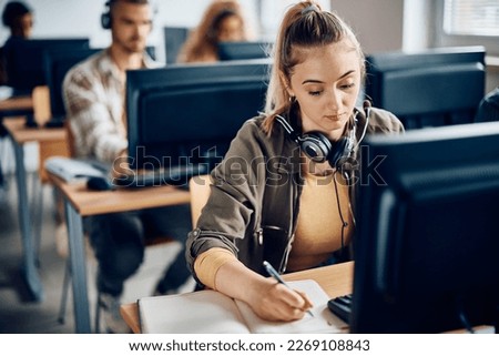 University student writing notes while e-learning on a computer in the classroom. Royalty-Free Stock Photo #2269108843
