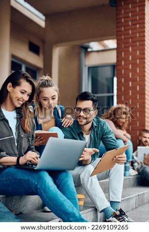 Happy college friends surfing the net on laptop at campus. Royalty-Free Stock Photo #2269109265