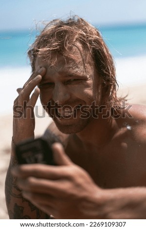 Man surfer puts zinc sun protection on his face.