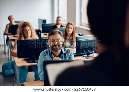 Matures man listening to a teacher while attending computer class in the classroom.  Royalty-Free Stock Photo #2269110459