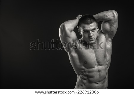 Muscular man bodybuilder with tattoos. Man posing on a black background, shows his muscles. Bodybuilding, posing, black background, muscles.