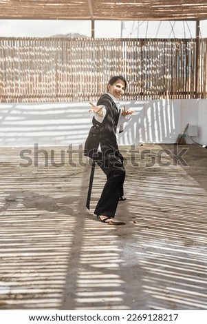 Self made brunette business woman in white shirt and black business suit filling positive emotions, smiling and enjoying the moment, dancing on bamboo terrace while relaxing on holiday vacation