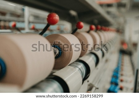 A close up of a yarn-spinning machine in a textile factory in China where the yarn bobins are created. A row of salmon colored bobbins are on display. Royalty-Free Stock Photo #2269158299