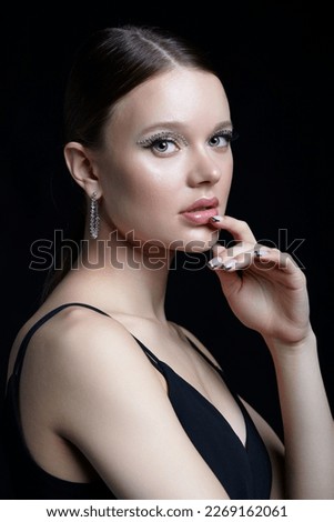 Female portrait with unusual rhinestones makeup. Woman with earring in the form of a shiny ring in the ear on black background. Hand near face Royalty-Free Stock Photo #2269162061