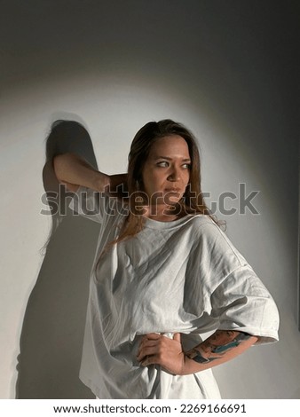 Young beautiful woman with long hair, green eyes in a white t-shirt, color tattoo on arm