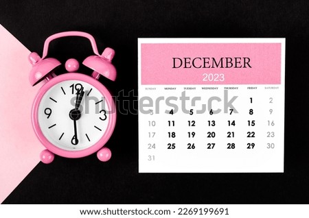 December 2023 Monthly calendar year with alarm clock on pink and black background.