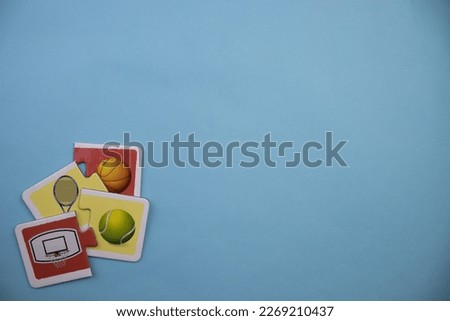 Colorfully colored puzzle pieces with pictures of tennis racket, tennis ball, basketball and hoop placed mixed in the lower left of the blue background.